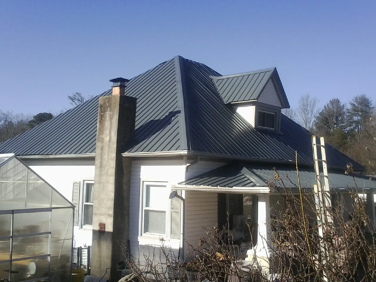 Dark blue standing seam metal roof on a white farmhouse with dormer — Slate & Tile Roof Repair by Roofing Brothers in Farner