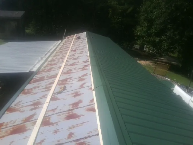 Old rusted panels beside newly installed green metal roofing — Wind Damage Roof Repair by Roofing Brothers in Farner