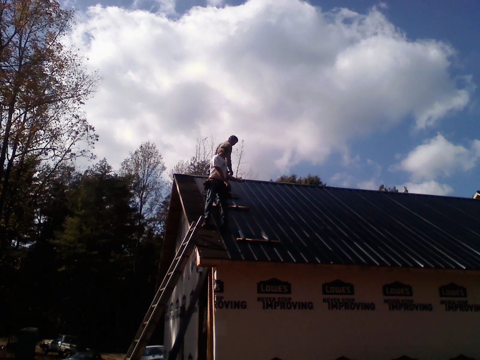 Roofer fastening dark metal panels high against a cloudy sky, from a Roof Inspection job in Farner