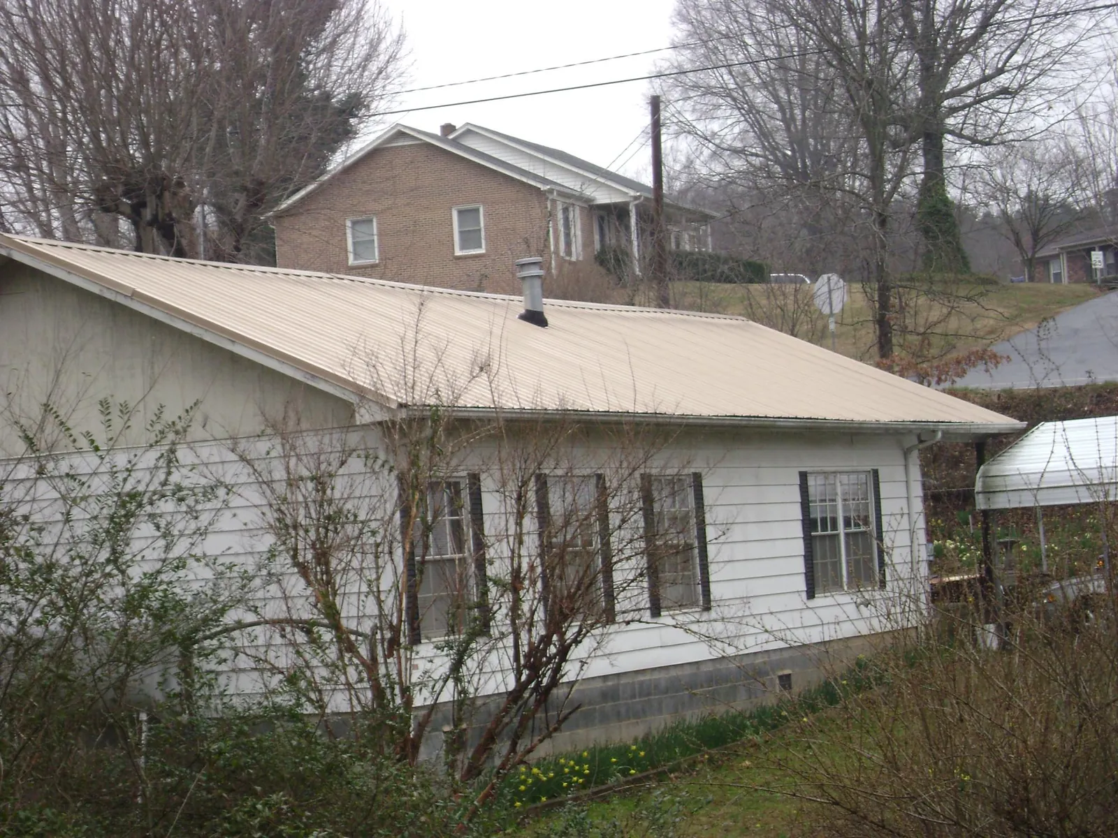 Tan metal roof on a white sided house set into a hillside — Commercial Roofing by Roofing Brothers in Farner